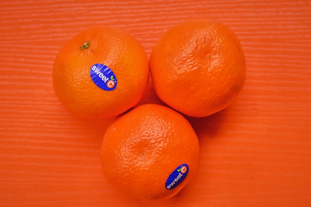 Close-up of three oranges with %22sweet c%22 stickers on an orange surface