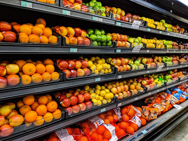 Grocery store produce aisle with shelves of fresh oranges and apples