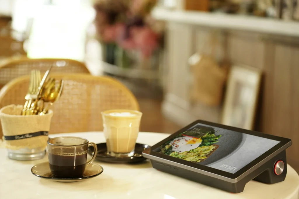 Barista at wooden counter using a tablet POS system in a cafe