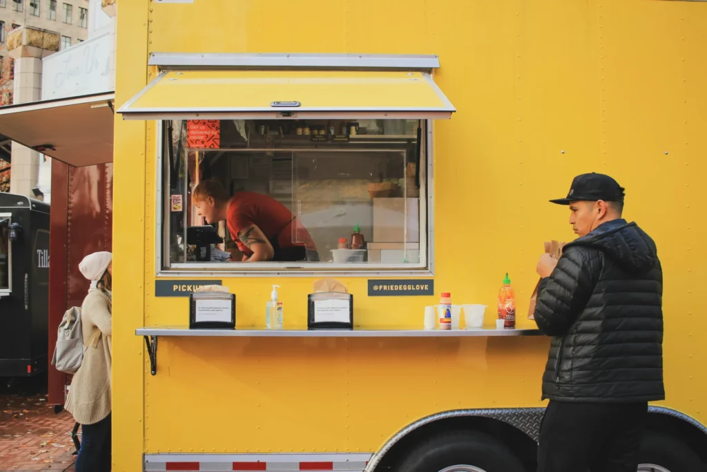 Customers waiting at the service window of a bright yellow food truck